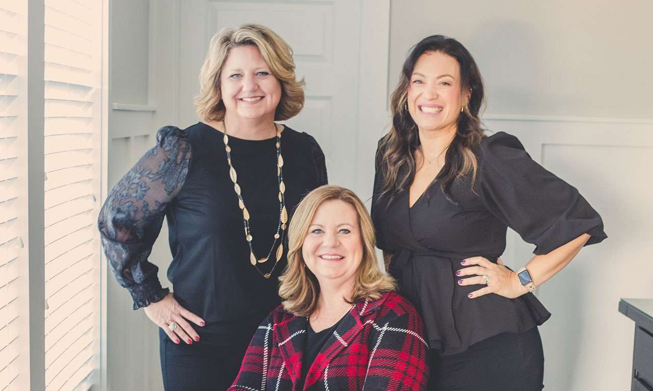 Three professional women smiling in office setting.