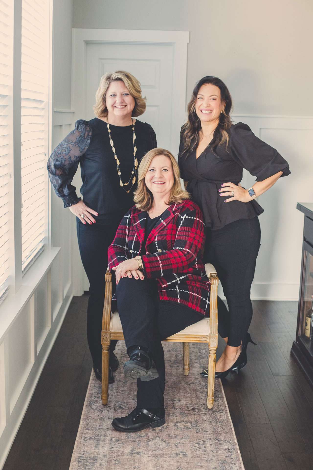 Three women smiling indoors, professional team portrait.